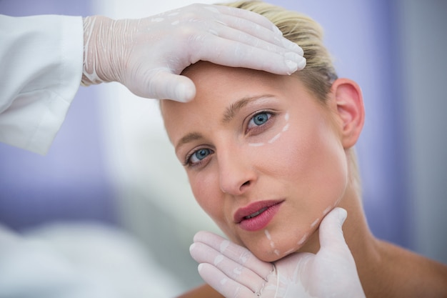 Arts die vrouwelijk patiëntengezicht voor kosmetische behandeling onderzoeken
