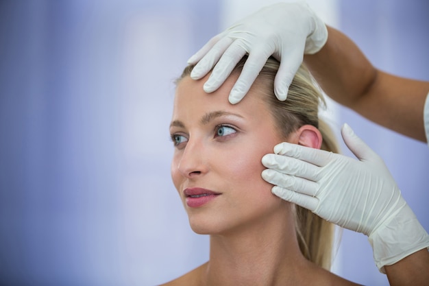 Arts die vrouwelijke patiënten gezicht van kosmetische behandeling onderzoeken