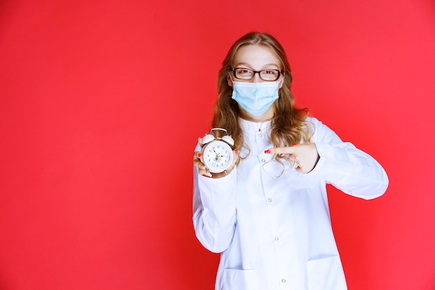 Gratis foto arts in gezichtsmasker die een klok toont die de tijd betekent voor het nemen van medicijnen.