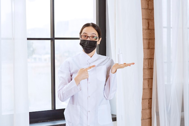 Arts in zwart masker en bril bij het raam staan en naar haar hand wijzend.