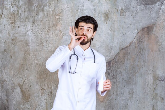 Arts met een stethoscoop die een witte tube handdesinfecterende spray vasthoudt en geniet van het product.