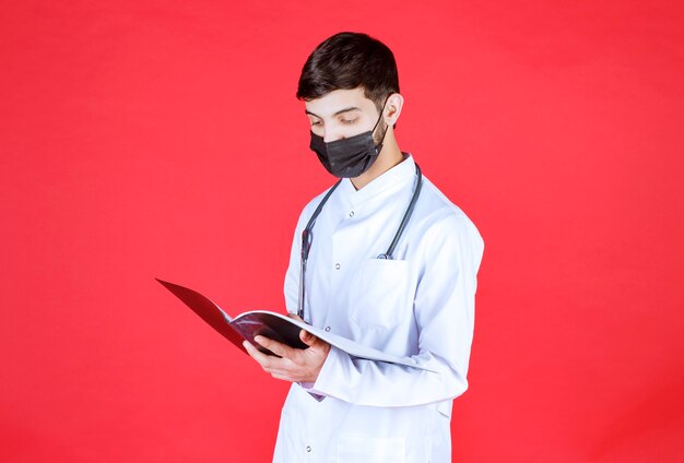Arts met een zwart masker die een zwarte map vasthoudt en leest.