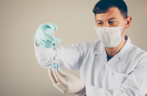 Arts met handschoenen en masker die de spuit in een flesje vullen. zijaanzicht horizontaal