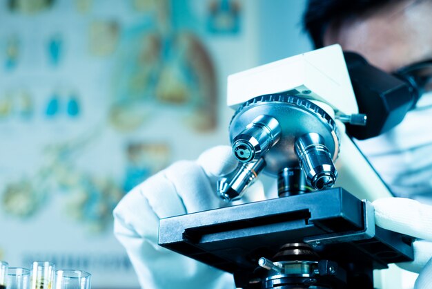 Arts of wetenschapper dragen medische gezichtsmasker en kijken in de microscoop tijdens het werken aan medisch onderzoek in wetenschappelijk laboratorium