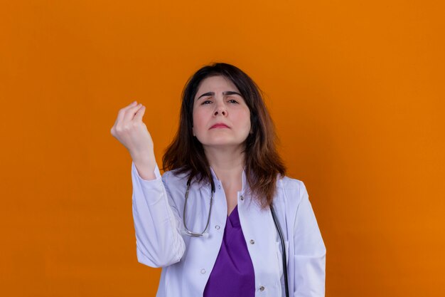Arts van middelbare leeftijd die witte laag draagt en met stethoscoop het gesturing met opgeheven hand die Italiaans gebaar over geïsoleerde oranje muur doet