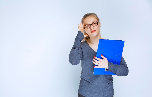 Assistent met bril die de blauwe map controleert en er attent en verward uitziet.