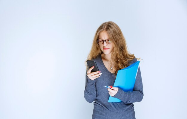 Assistent met bril die een blauwe map vasthoudt en tegen de telefoon praat.