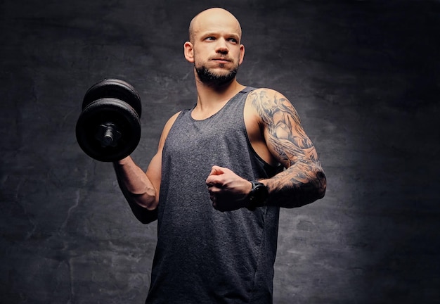 Atletisch geschoren hoofd getatoeëerd man doet biceps training met halter.