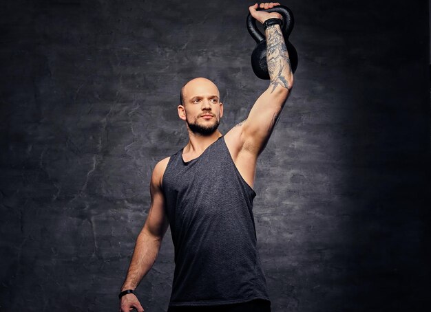 Atletisch geschoren hoofd getatoeëerd mannetje doet schoudertraining met de Kettlebell.