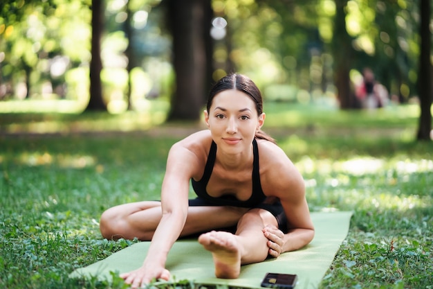 Atletische jonge vrouw doet yoga in het park in de ochtend, de opleiding van vrouwen op een yogamat