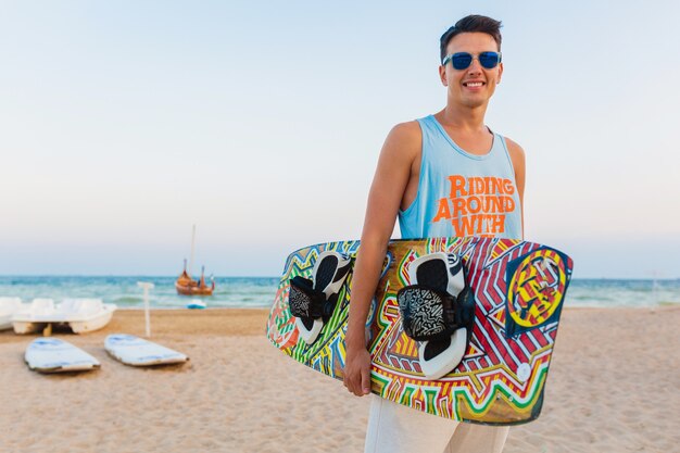 Atletische jongeman met kitesurfen bord poseren op strand zonnebril dragen op zomervakantie