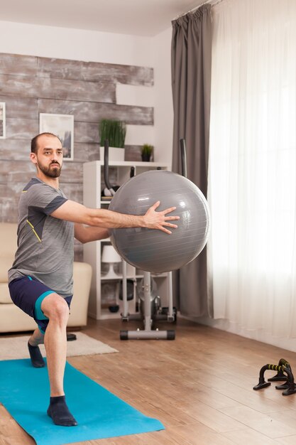 Atletische man doet lunges training met Zwitserse bal tijdens zelfisolatie.