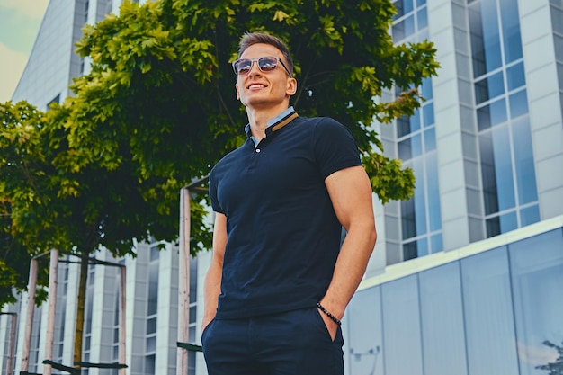 Atletische stijlvolle man in zonnebril over modern gebouw achtergrond.