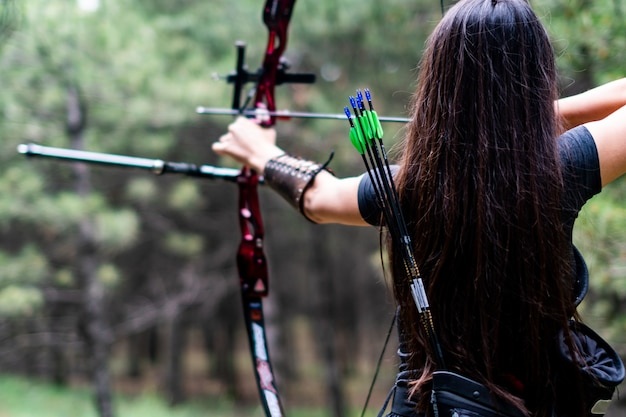 Atletische vrouw die met pijl en boog naar de bomen mikt