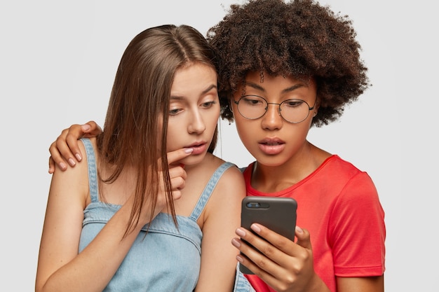 Attente, nieuwsgierige vrouwtjes van gemengd ras lezen iets op de smartphone