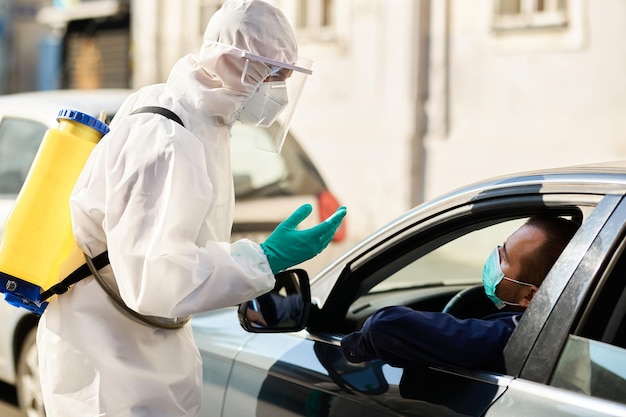 Automobilist en gezondheidswerker in beschermend pak praten bij de controlepost van de stad tijdens de COID19-epidemie