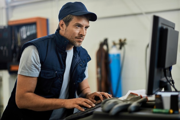 Automonteur die computer gebruikt terwijl hij in een autoreparatiewerkplaats werkt