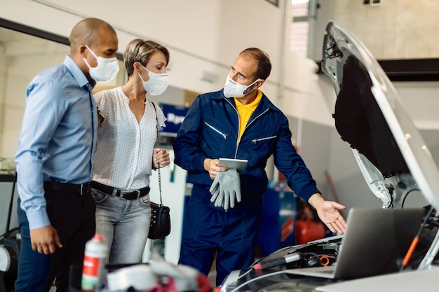 Gratis foto automonteur en zijn klanten praten tijdens het onderzoeken van autopech in een werkplaats tijdens de coronaviruspandemie