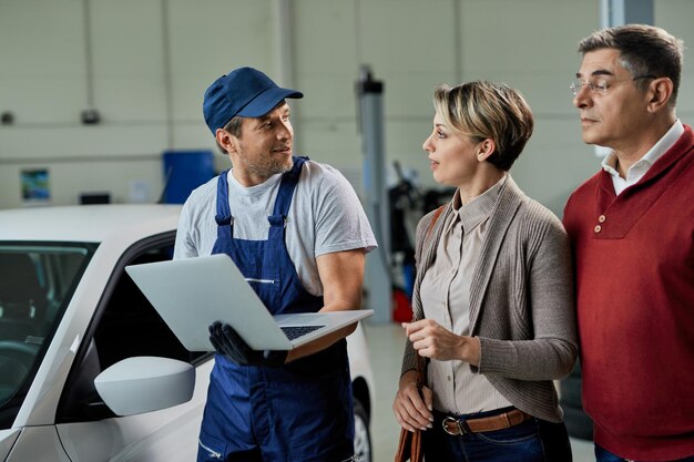 Autoreparateur die met zijn klanten communiceert terwijl hij laptop in een werkplaats gebruikt