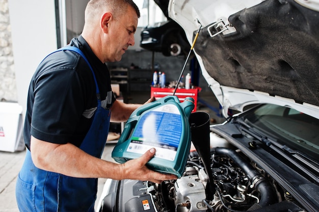 Autoreparatie- en onderhoudsthema Monteur in uniform werken in autoservice die nieuwe motorolie giet