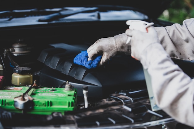 Autowasserettearbeider die een witte eenvormig dragen die zich een spons bevinden om de auto in het autowasserettecentrum schoon te maken, concept voor de autozorgindustrie.