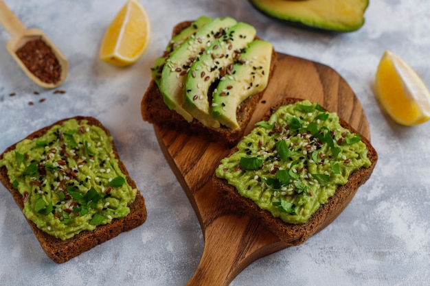 Avocado open toast met plakjes avocado, citroen, lijnzaad, sesamzaadjes, plakjes zwart brood, bovenaanzicht