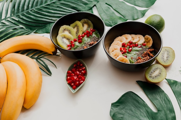 Avocado-smoothiekom met daarop chia, granola, kiwi en spinazie. Overhead, bovenaanzicht, plat gelegd. Gezond ontbijt. Tropische bladeren.