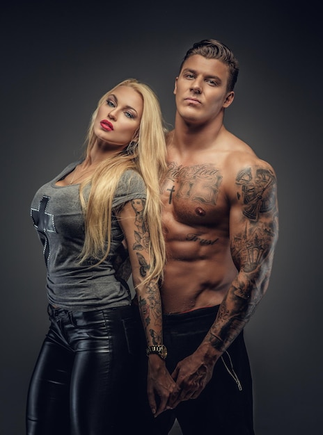 Awesome blonde vrouw poseren met shirtless gespierde getatoeëerde man. geïsoleerd op grijze achtergrond.
