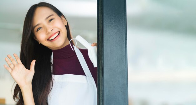 Aziatisch aantrekkelijk vrouwelijk cafépersoneel draagt uniform schort glimlachend vrolijk welkom in café-restaurant met zelfvertrouwen en geluk met positieve servicegeest nadat de afsluiting voorbij is bij de ingang van de winkel