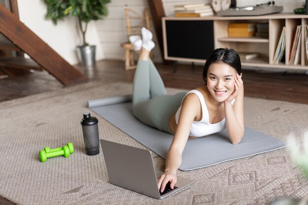 Aziatisch fitnessmeisje dat online fitnesscursus volgt en naar sportvideo's kijkt die thuis oefenen op de vloer...