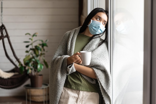 Aziatisch meisje met medisch gezichtsmasker verlangt ernaar naar buiten te gaan, ziek te zijn van covid en op zichzelf te blijven...