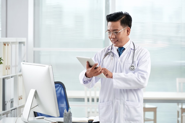 Aziatische arts die medische app op zijn digitaal apparaat gebruikt