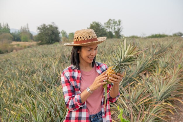 Aziatische boerin ziet de groei van ananas in boerderij, jonge mooie boer vrouw staande op landbouwgrond.