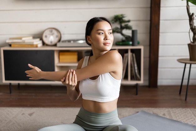 Aziatische fitness meisje doet training thuis zittend op de vloermat in activewear opwarmen en een...