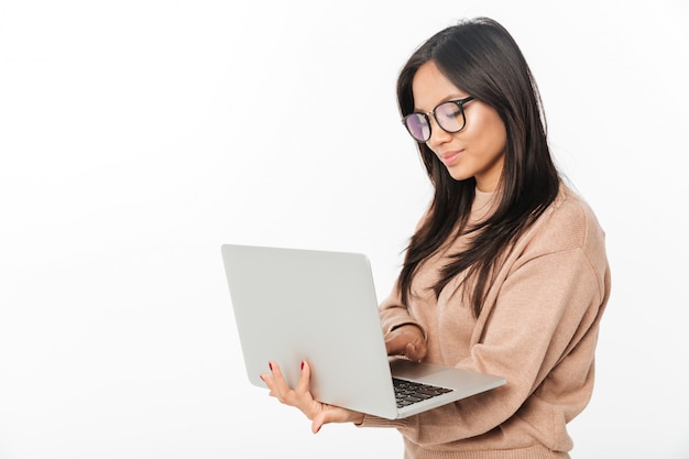Aziatische glimlachende vrouw die glazen draagt die laptop met behulp van
