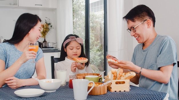 Aziatische Japanse familie ontbijt thuis. Aziatische moeder, vader en dochter voelen zich gelukkig samen praten terwijl brood, cornflakes granen en melk in kom op tafel in de keuken in de ochtend eten.