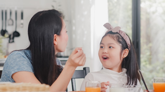 Aziatische Japanse familie ontbijt thuis. Het Aziatische mamma en dochter gelukkige samen spreken terwijl het eten van brood, drinkt jus d'orange, cornflakesgraangewas en melk op lijst in moderne keuken in ochtend.