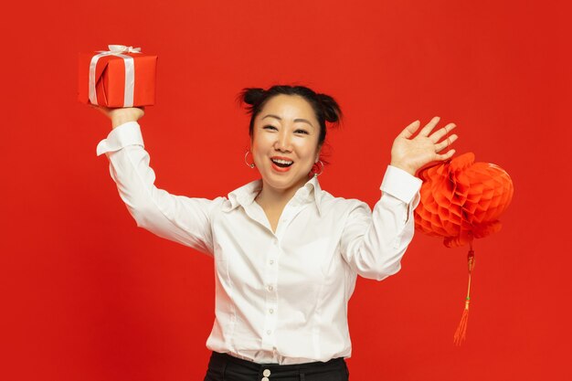 Aziatische jonge vrouw met lantaarn en cadeau op rode muur
