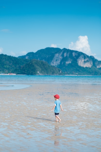 Aziatische jongen die op het strand in zee en blauwe hemel loopt