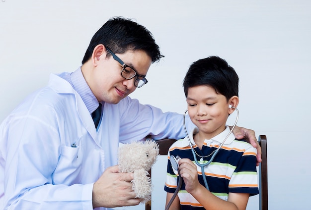 Aziatische jongen en arts tijdens het onderzoeken van het gebruiken van stethoscoop over witte achtergrond