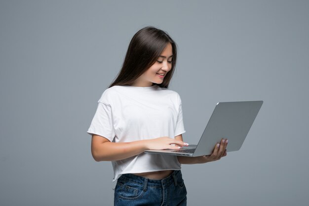 Aziatische laptop van de vrouwenholding computer terwijl het bekijken de camera over grijze achtergrond