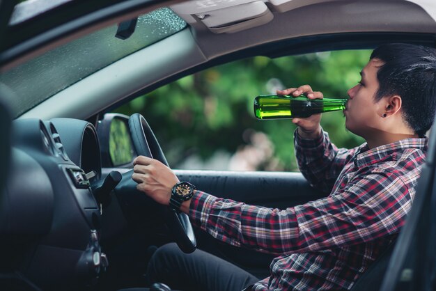 Aziatische man drinkt een bierfles terwijl het besturen van een auto