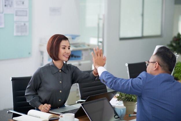 Aziatische man en vrouw in bedrijfskledij aan tafel zitten in de vergaderzaal en het doen van high-five