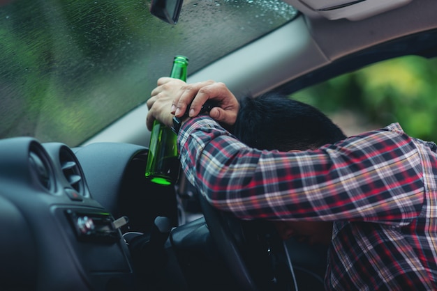 Gratis foto aziatische man houdt een bierfles terwijl het besturen van een auto