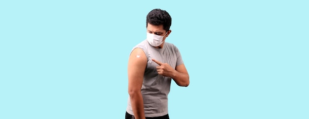 Aziatische man toont zijn gevaccineerde arm op blauwe achtergrond in studio met kopieerruimte