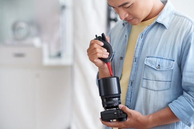 Aziatische mannelijke phographer schoonmakende cameralens met luchtventilator