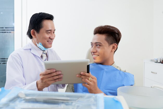 Aziatische mannelijke tandarts met tablet raadplegende patiënt in kliniek