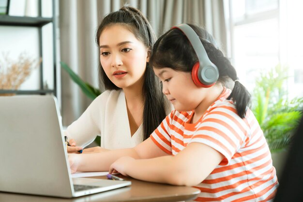 Aziatische moeder geniet van het leren en uitleggen van huiswerk aan kinddochter voor online studie tijdens thuisonderwijs thuis thuisquarantaine online leren nieuwe normale levensstijl