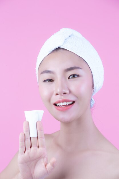 Aziatische mooie vrouw die het gezicht op een roze achtergrond, de Kosmetiek en het Kuuroord afvegen.