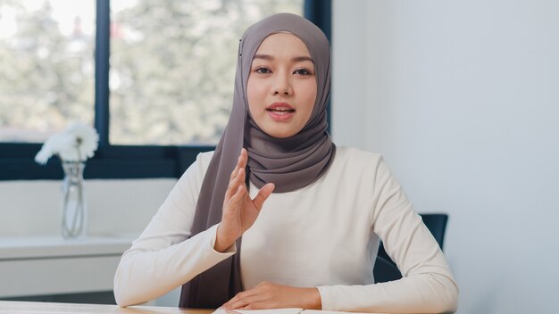 Aziatische moslimdame die naar de camera kijkt, praat met collega's over het plan in een videogesprek in een nieuw normaal kantoor.
